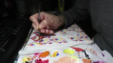 A closeup of a person drawing colorful patterns in a dark room illuminated with a lamp