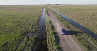 An aerial view of a pick-up driving down a rural dirt road near a stream