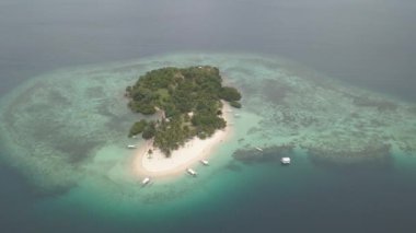 An aerial view of boats with stabilizer floats near a tropical island with sandy beaches in the middle of the ocean