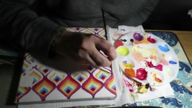 A closeup of a person drawing colorful patterns in a dark room illuminated with a lamp