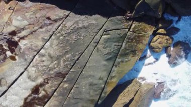 An aerial view of people on a rocky high ground by the sea while waves hitting rocks