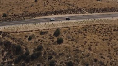 An aerial footage of two cars traveling on a deserted highway