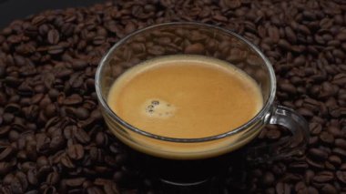A closeup of a rotating cup of coffee on a pile of coffee beans