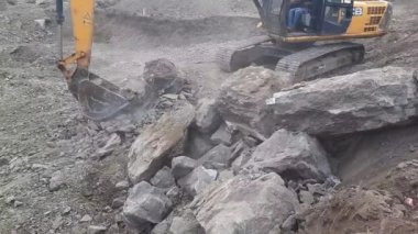 An Excavator's arm picks up the big rocks. A hydraulic excavator works for the construction of new building land.