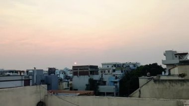 A time-lapse of the pastel sunset clouds moving over an old residential area until the night