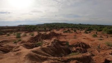A panoramic view of a sandy landscape with mounds and green bushes