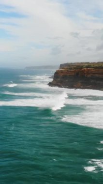 A vertical aerial drone shot of the ocean waves washing the cliffs and shore of Ericeira, Portugal