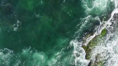 The drone footage of the green ocean waves and people on the rocky shore.