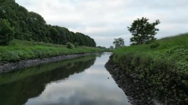 A drone footage of a narrow river passing through fields and forest
