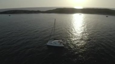Bir adanın yakınındaki dalgalı okyanus suyundaki beyaz bir geminin havadan görüntüsü.