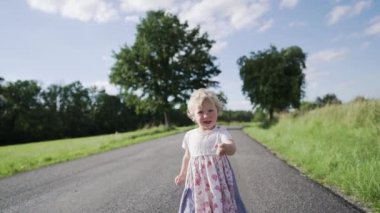 A cute little Caucasian baby girl walking on a rural road