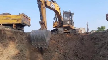 An excavator is digging and cutting construction land. And the tractor and dumper truck is standing left and right to carry the soil moorum on the c