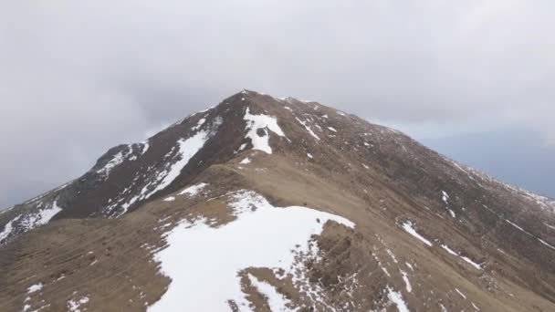 無人機によって示される溶かされた雪の乾燥した山の頂上に立つ男 — ストック動画