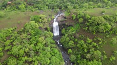 An aerial view of waterfall in the middle of green trees in the forest
