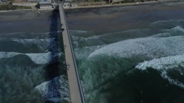 A Drone shot La Jolla Shores with wavy ocean and a view of coastal houses under a blue cloudy sky