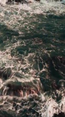 A vertical aerial shot of stormy sea waves against rocks in Hong Kong