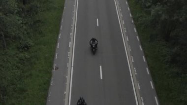 A high angle HD drone footage of motorbikes racing on an asphalt road in the middle of trees