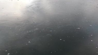 A drone flies over a frozen lake with lumps of ice on it. You can see reflections on the ice. At the end you can still see part of the landscape.