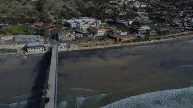 A Drone shot La Jolla Shores with wavy ocean and a view of coastal houses under a blue cloudy sky