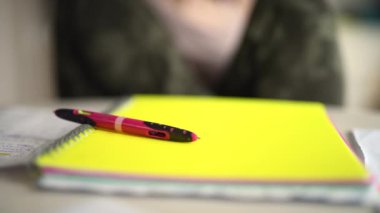 A closeup of a Caucasian female sitting at the table, against a yellow notebook and a pen