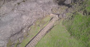 A drone shot over a rocky hill with a green moss growth and a beautiful river going between the rocks