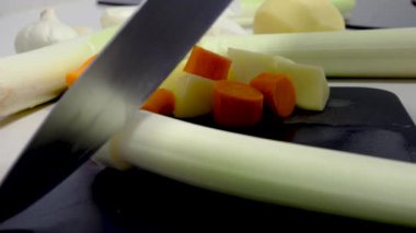A cutting board with vegetables and a knife cutting leek in slow motion