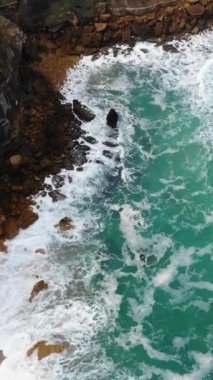 the Vertical drone top shot of the ocean turquoise waves foam touching the cliff rocks, Ericeira, Portugal
