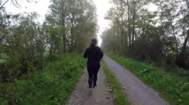 A caucasian woman running through a forest path