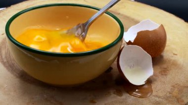 A cook beating the eggs with a fork in a yellow bowl