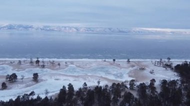 An aerial drone footage of the frozen lake and the icy beach at the foot of the snowy mountains