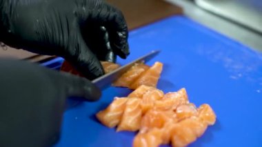 A closeup shot of man's hands in black gloves cutting a piece of salmon into pieces