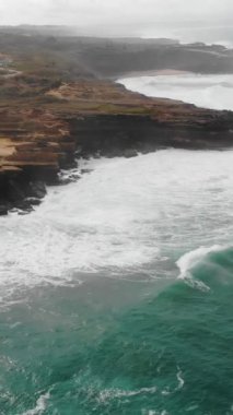 A vertical aerial drone shot of the ocean waves washing the shore of Ericeira, Portugal