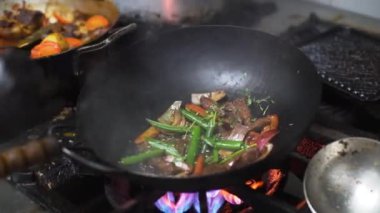 A man's hands, with a frying pan with meat and vegetables inside, in slow motion, on high heat in an industrial kitchen
