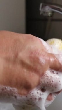 A vertical footage of a hand washing a dish in the sink in the kitchen