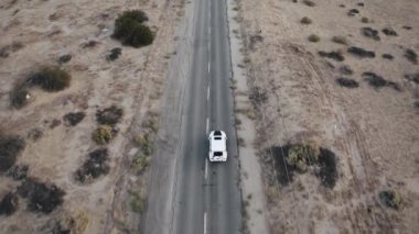 An aerial shot of a car driving on a road surrounded by a desert
