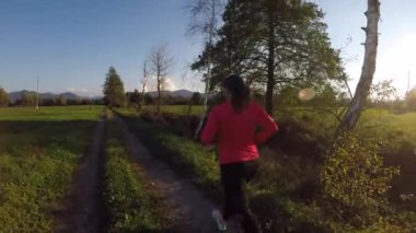 A Side shot of a young female with a sportive outfit running in narrow road between green fields