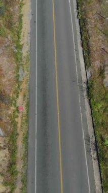 A vertical aerial drone footage of a road passing through a mountain