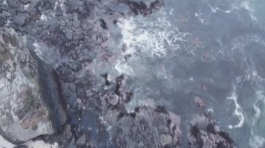 A top view of the waves crashing into the rocky cliffs on the coast