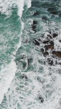 A vertical aerial drone footage of the big waves of washing the beach in Ericeira, Portugal