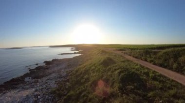 A scenic drone footage of a body of water near the forested shore during sunrise and a biker riding on a narrow path
