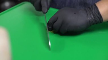 A closeup shot of a person in black gloves cutting parsley on a green cutting board