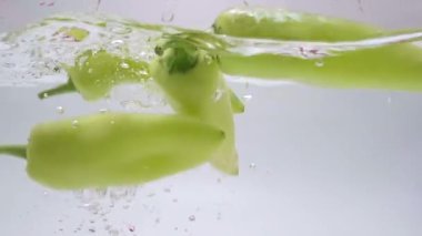 An HD of the green peppers dropping down into water with white background