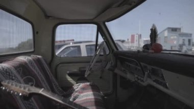 The interior of an old vintage truck, with a guitar sitting in the passenger seat
