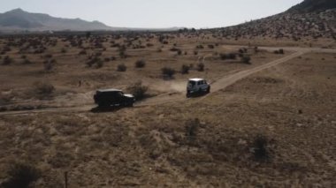 A Drone shot of black and white Mercedes G Wagon cars driving through desert area