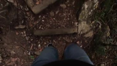 A POV footage of a man in shorts climbing the trail in forest with fallen leaves