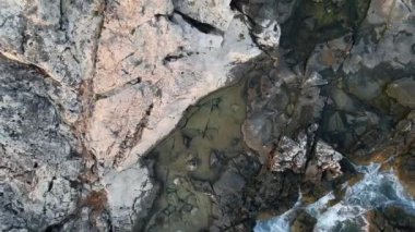 An aerial top view of waves crashing on a rocky coast with cliffs