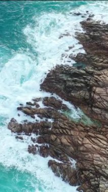 An aerial view of ocean waves splashing on a rough cliff in Australia