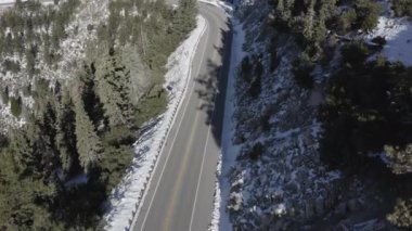An aerial view of an empty highway asphalt road surrounded by snow-capped mountains