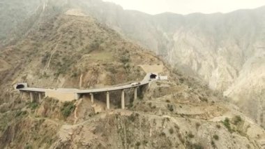 Uzun kayalık dağlar ve tünele giren arabalar arasındaki bir yolun havadan görüntüsü.