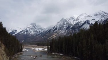 Arka planda şelaleye dönüşen bir nehrin ve karlı dağların manzarası.